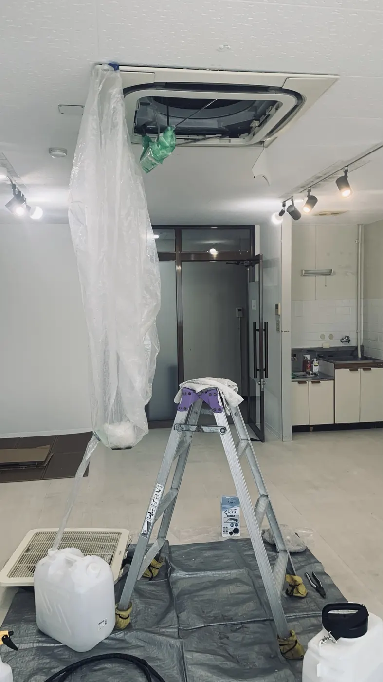 事務所の天井埋込4方向エアコン。パネルを外し、洗浄カバーを垂らして床に排水用のポリタンクを置いている