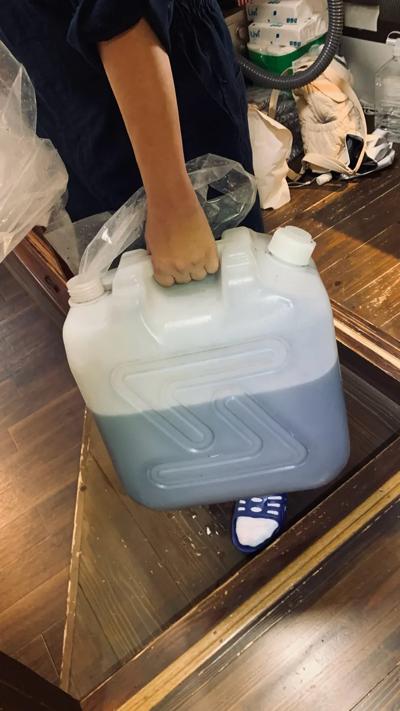 洗浄後の汚れた水がたまった白いポリタンクを手に持っている